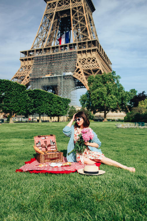 Mujer sentada en la grama con una cesta y mantel lista par un picnic con la torre Eiffel de fondo Mujer sentada en la grama con una cesta y mantel lista par un picnic con la torre Eiffel de fondo